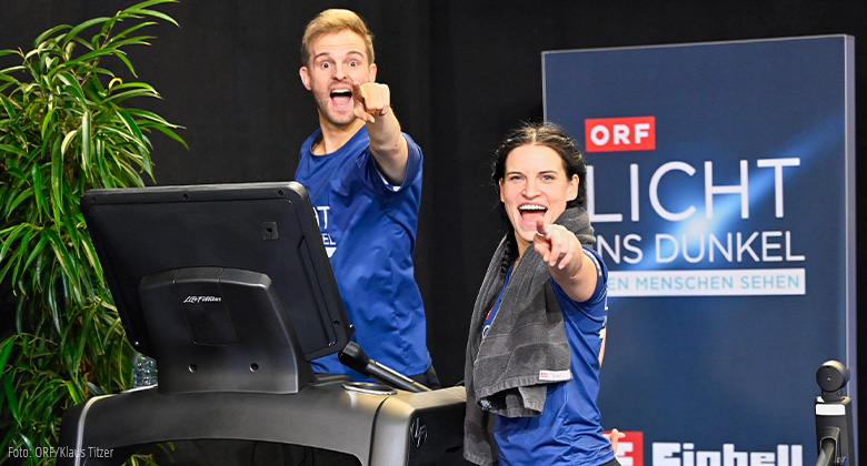A man and a woman on a treadmill in sportswear point enthusiastically at the camera, ORF logo in the background.