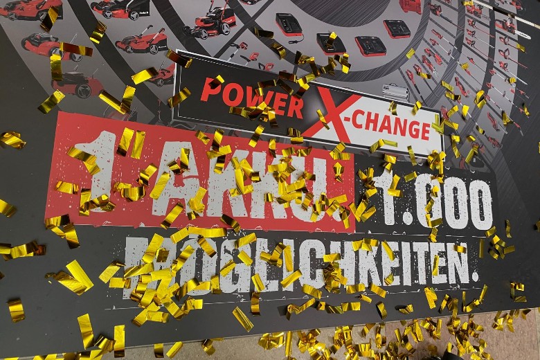 Einhell Power X-Change sign with "1 Akku – 1,000 Möglichkeiten" and gold confetti.