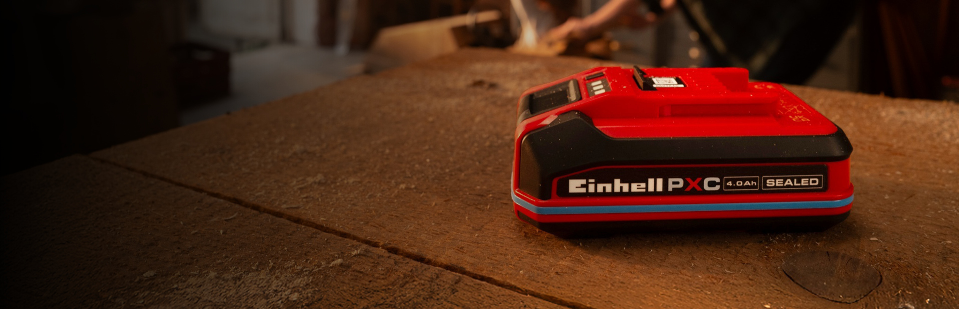 Einhell Power X-Change Akku 4.0Ah SEALEAD auf einer Werkbank aus Holz, mit blauem Ring und sichtbarem Label.