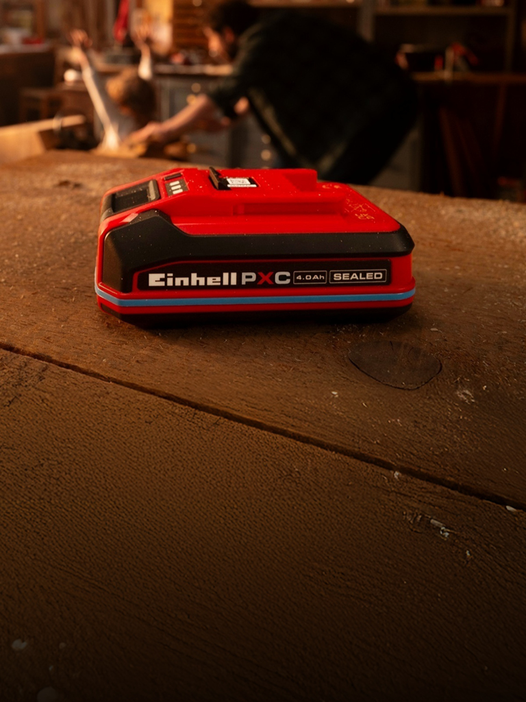 Einhell Power X-Change Akku 4.0Ah SEALEAD auf einer Werkbank aus Holz, mit blauem Ring und sichtbarem Label.