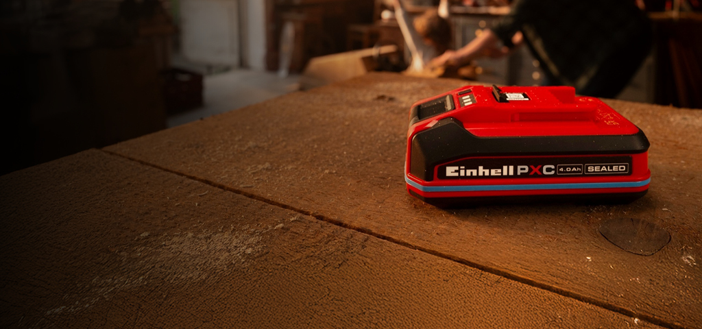 Einhell Power X-Change Akku 4.0Ah SEALEAD auf einer Werkbank aus Holz, mit blauem Ring und sichtbarem Label.