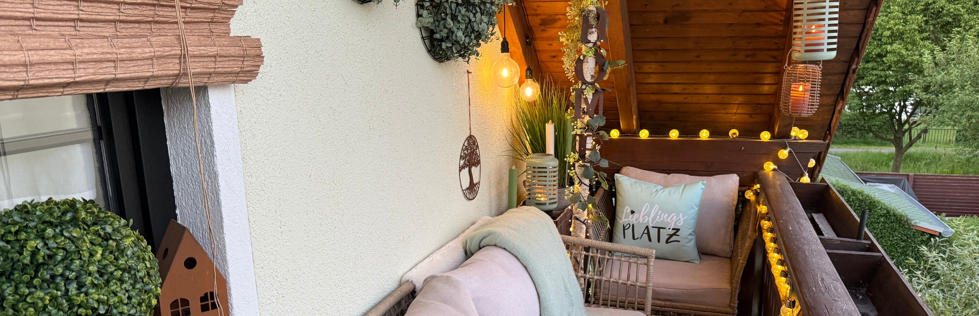 Eine stilvoll eingerichtete Balkon-Lounge am Abend, beleuchtet durch warme Lichterketten, Laternen und Glühbirnen.