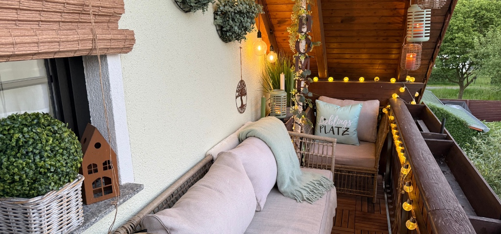 Eine stilvoll eingerichtete Balkon-Lounge am Abend, beleuchtet durch warme Lichterketten, Laternen und Glühbirnen.