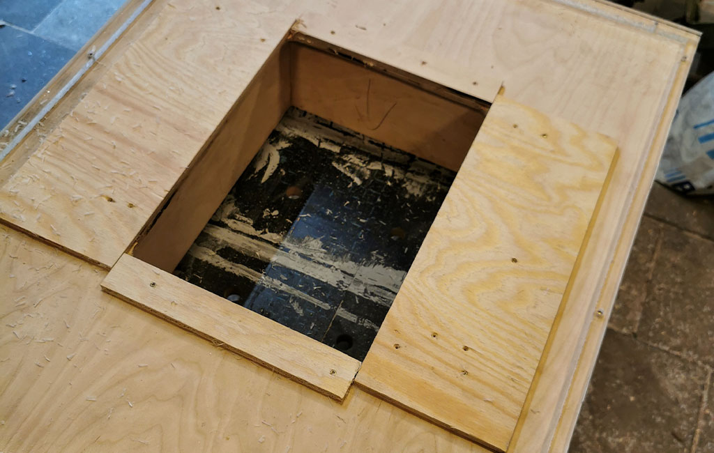 Nahaufnahme einer Holzplatte mit zentralem quadratischen Ausschnitt, befestigt mit Schrauben.