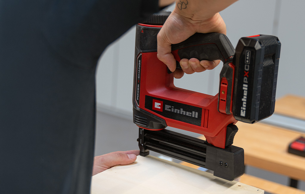 A person uses an Einhell cordless nailer to fasten a wooden board.