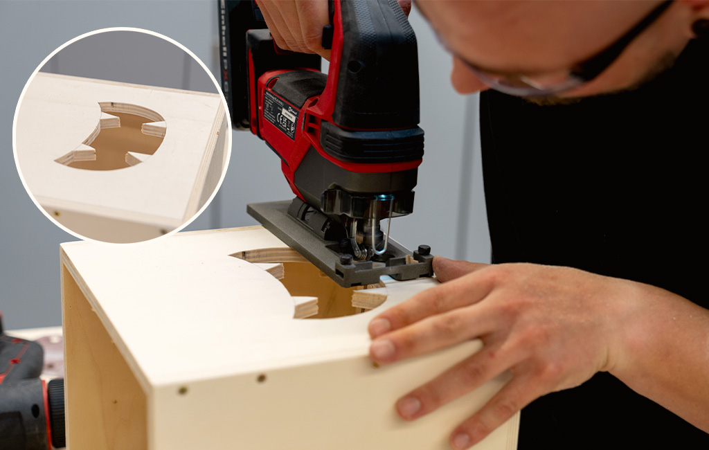 A person uses an Einhell cordless jigsaw to cut a jagged shape into a wooden panel; the inset shows the cutout.