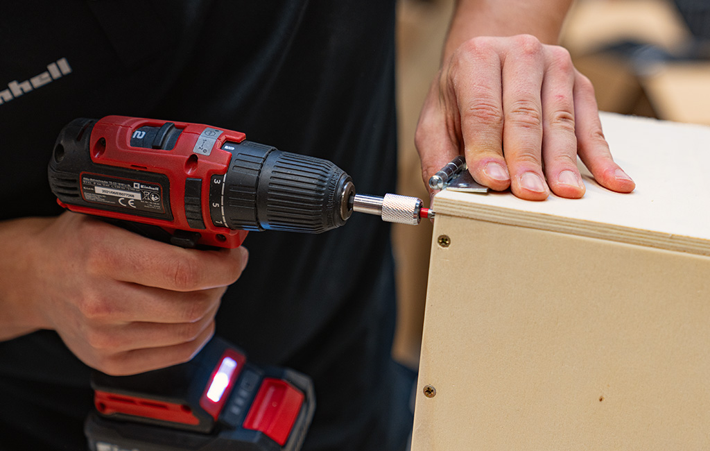 A person uses an Einhell cordless drill driver to screw together the corner of a wooden box.