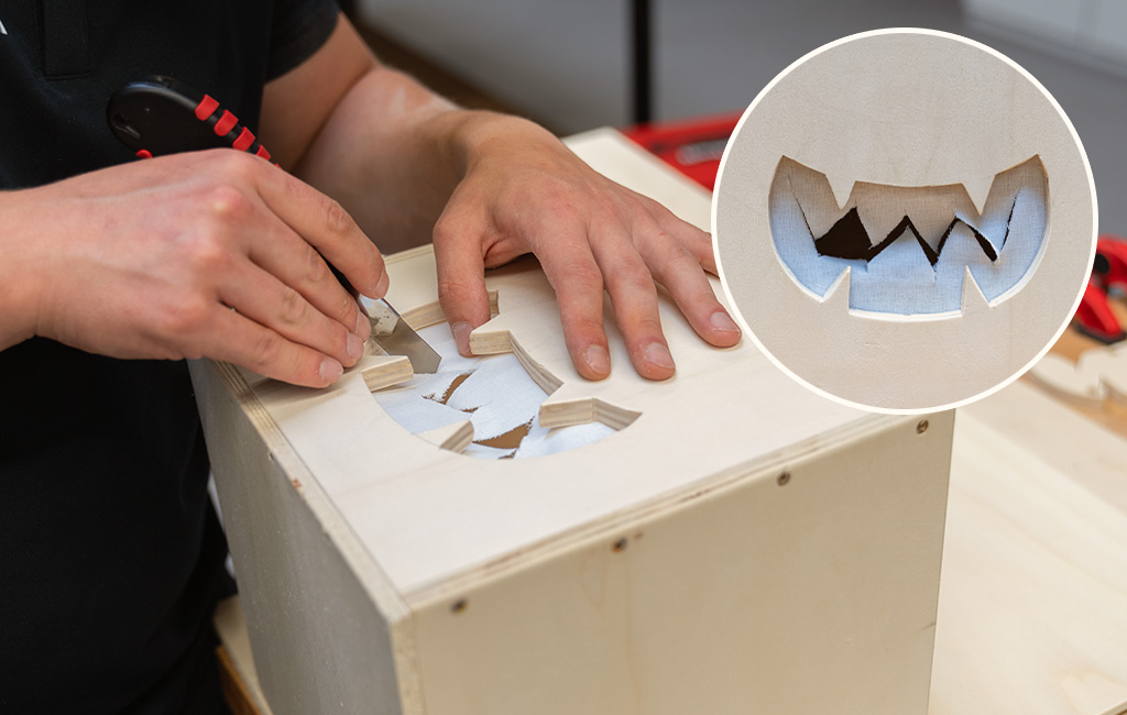 A person files the edges of a jagged cutout in a wooden box; the inset shows the finished shape.