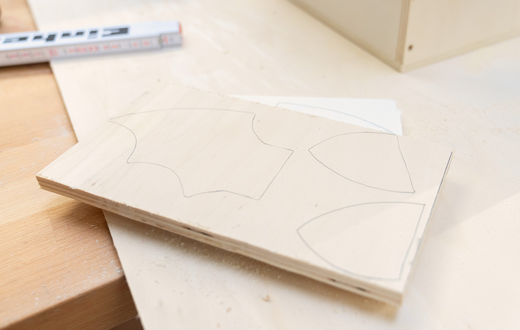 A wooden board with several curved shapes drawn on it, ready to be cut.
