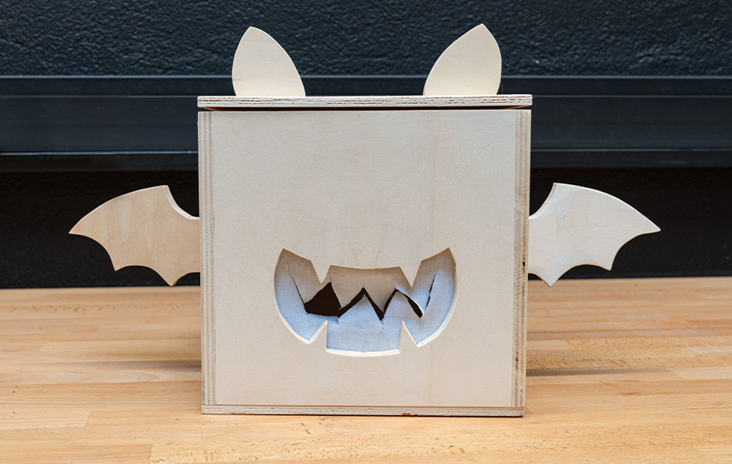A finished wooden box decorated as a bat, with wings, ears and a cut-out face.