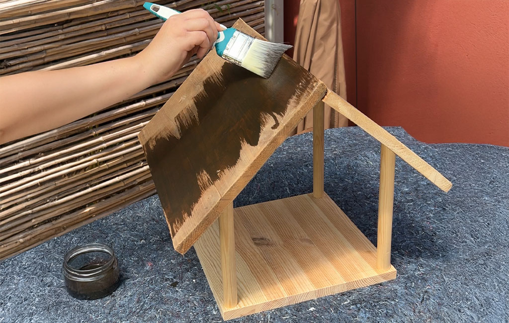 The roof of the bird feeder is being painted dark with a brush.