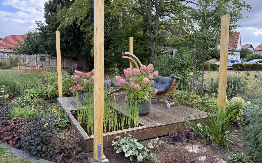 Holzpfosten, die auf einer erhöhten Gartenplattform als erster Teil einer Pergola angebracht wurden.