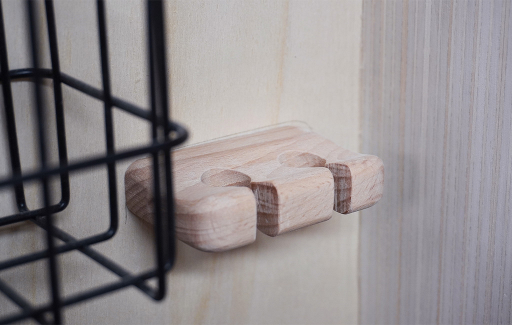 Kleiner Halter aus Holz mit Aussparungen, montiert neben einem schwarzen Drahtkorb.