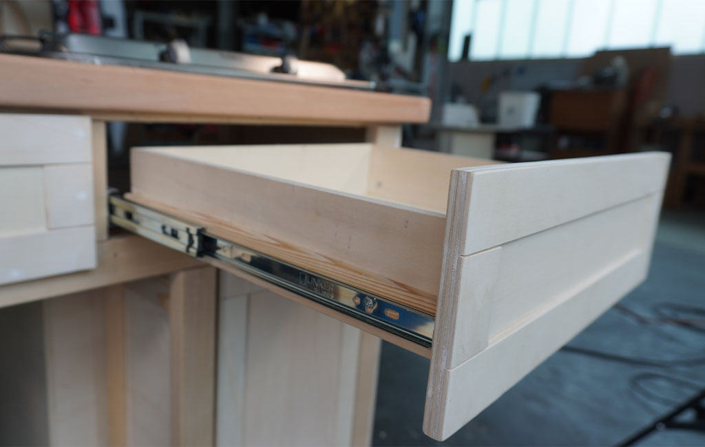 Geöffnete Schublade aus hellem Holz in einer Küchenzeile mit Metallschienen zum Ausziehen.