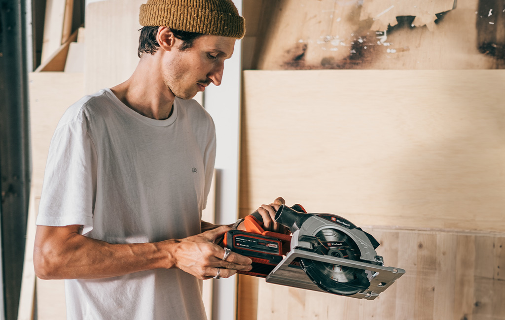 Person in a white shirt holding an Einhell circular saw, inspecting the tool.