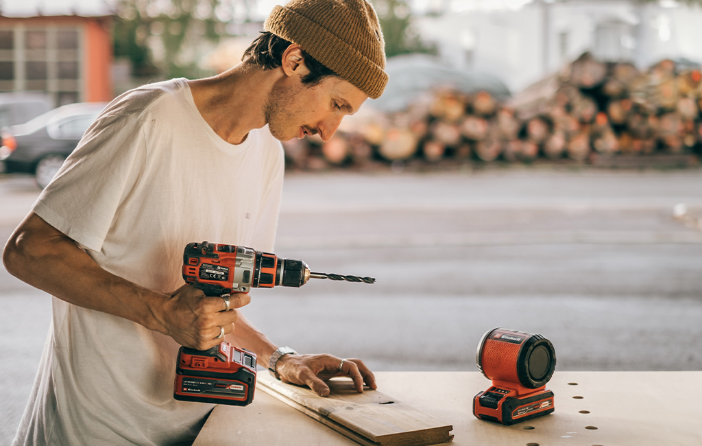 Person drilling holes in a wooden board with an Einhell cordless drill on a workbench.