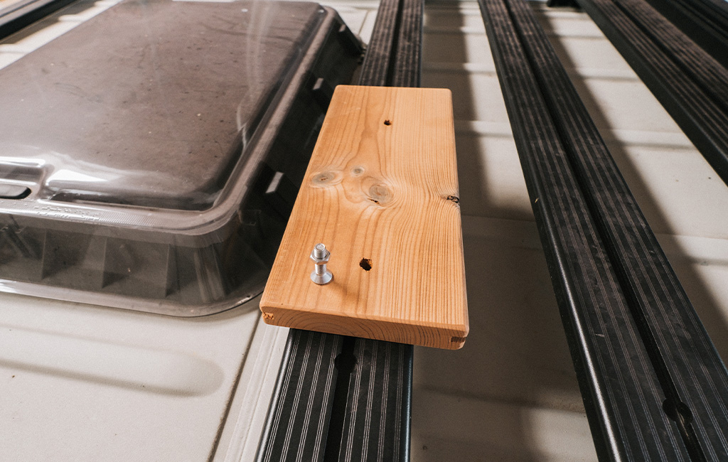 Close-up of a wooden board with screws on a black metal frame on the camper roof.