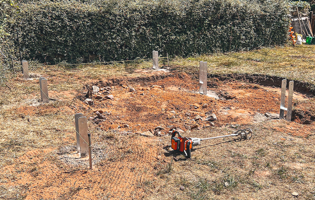 Construction site with six metal post bases and tools on the ground, string stretched for alignment.