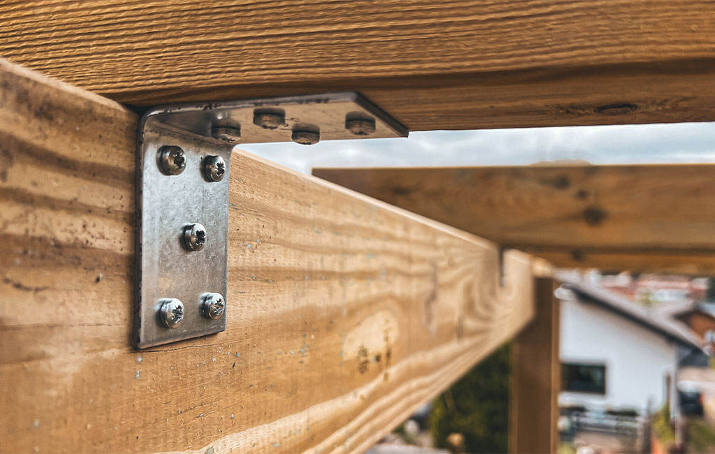 Close-up of a metal bracket with screws connecting two wooden beams.