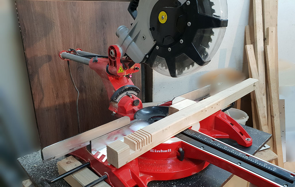 An Einhell sliding mitre saw is set on a workbench, a wooden beam is clamped ready for cutting.