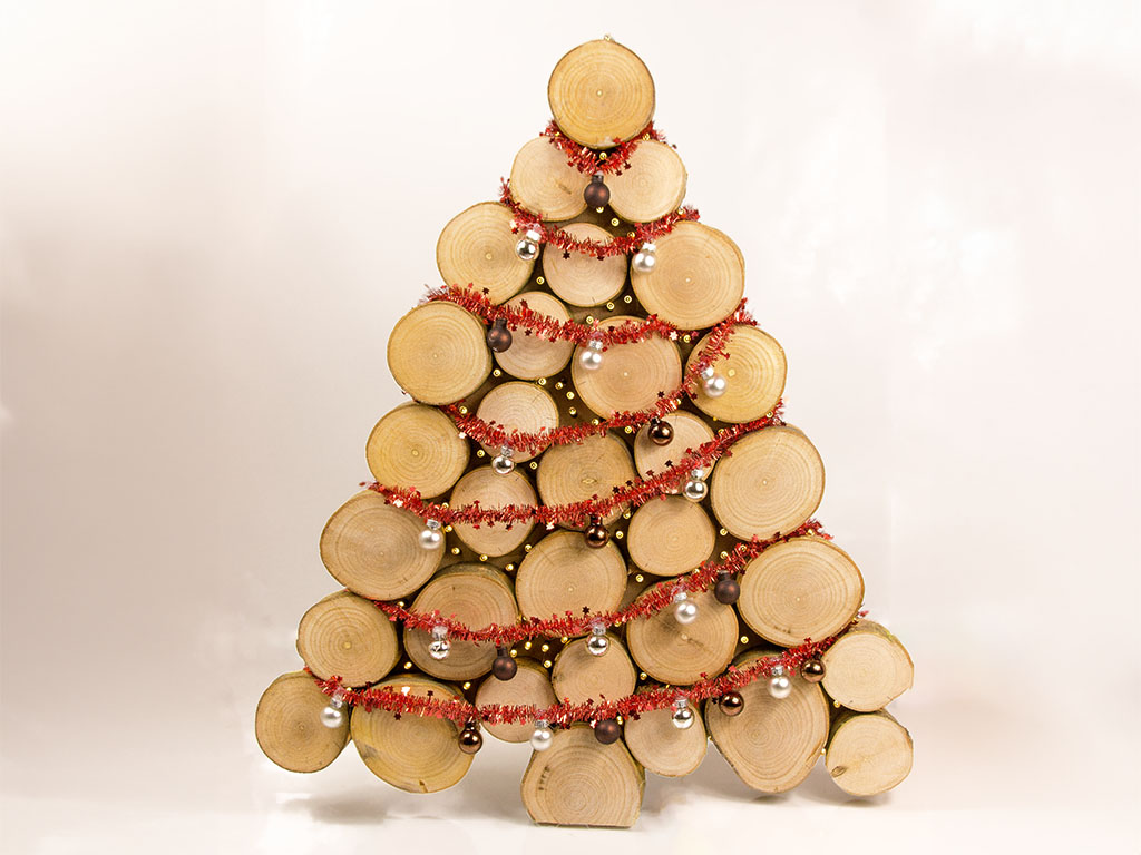 Christmas tree made of wooden discs with red garland and silver baubles in front of a white background.
