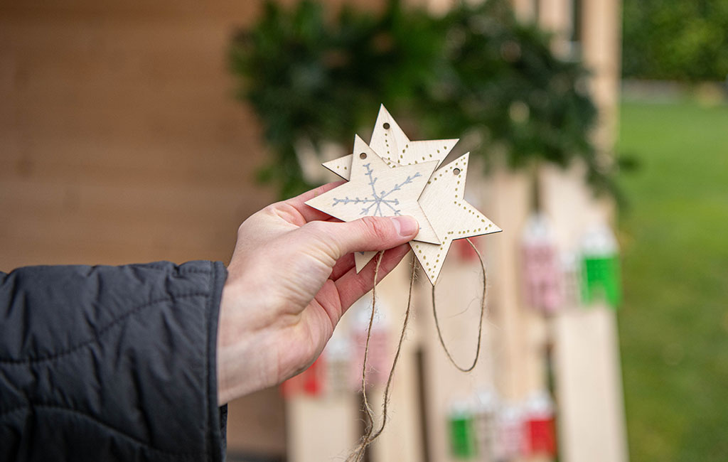 A hand shows three wooden stars with snowflake design, with a decorated pallet in the background.