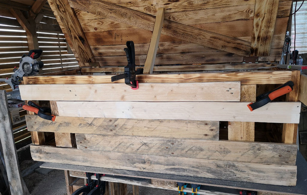A wooden chest under construction. Several wooden boards are clamped to the front with screw clamps.