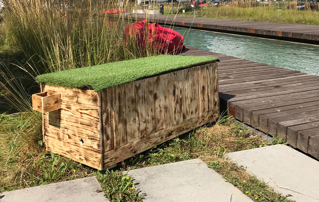 The finished wooden chest with an artificial grass lid stands on a lawn next to a wooden walkway.
