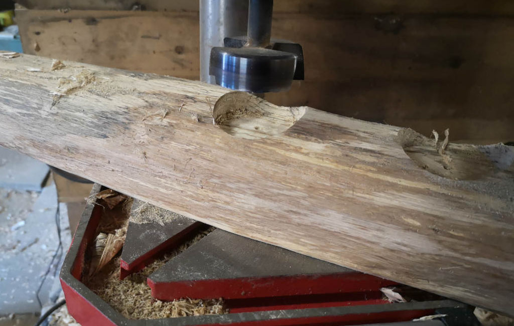 Mit einer Tischbohrmaschine werden Löcher in ein Holzbrett für ein DIY-Weihnachtsdeko-Projekt gebohrt.