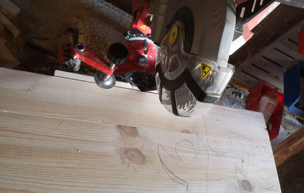 Aus einem Holzbrett wird mit einer Kreissäge die vorgezeichnete Form geschnitten.