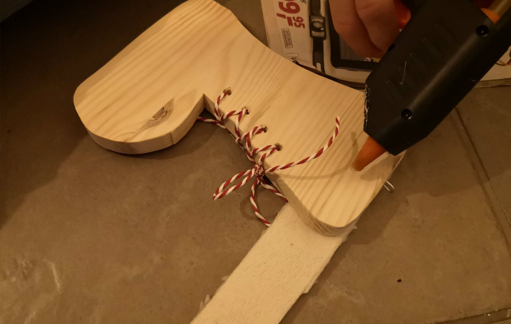 Mit einer Heißklebepistole wird rot-weiße Schnur an einem Holzstiefel befestigt.