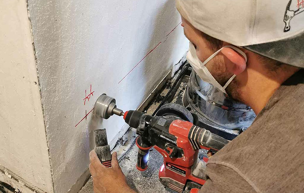 Person drills a hole into a wall using a drill, with dust forming at the drilling point.