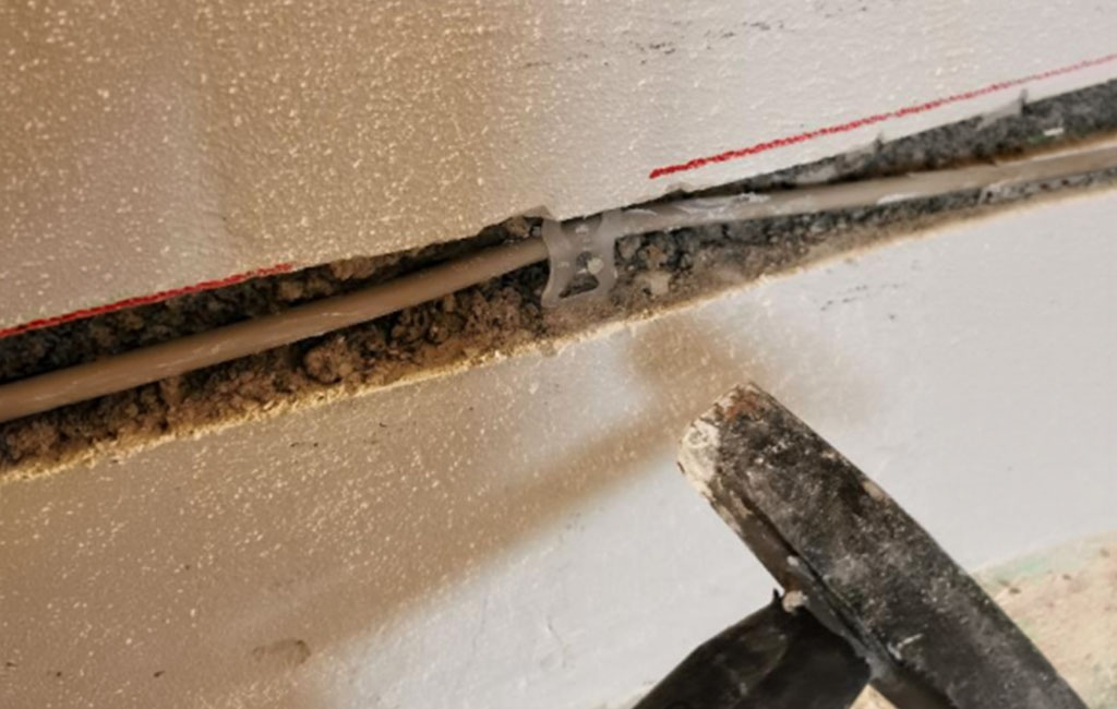 Close-up of a milled wall groove where a cable is being installed, with dust and plaster debris along the edge.