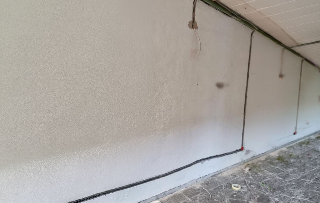 Long milled wall groove near the ceiling with cable already installed; protruding cable has been cut off, dust on the floor.