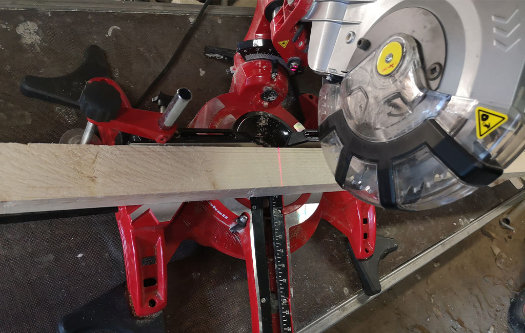 An Einhell miter saw cuts a wooden board, a red laser shows the cutting line.