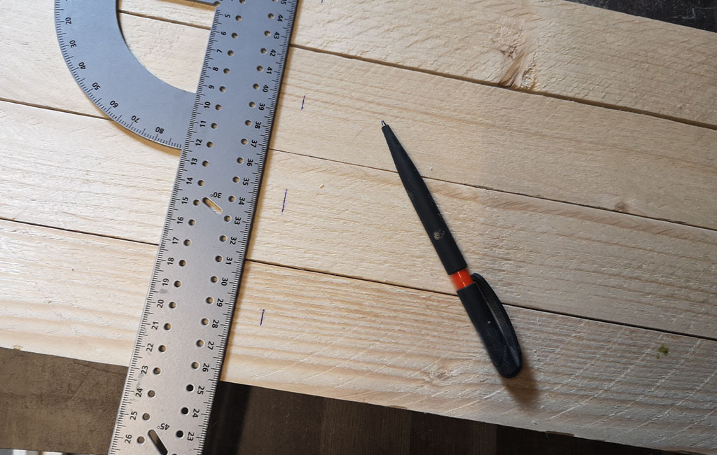 A ruler and pen lie on several wooden slats, markings are visible on the wood.