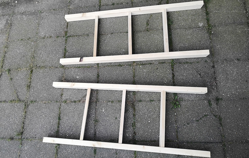 Two finished wooden frames with crossbars lie next to each other on a paved ground.