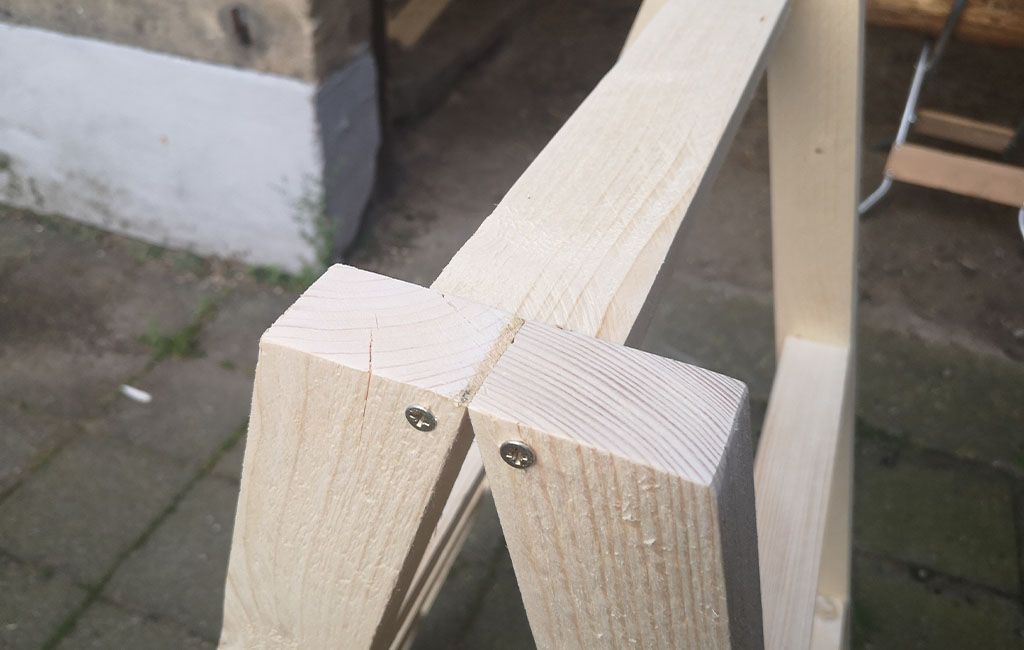 Two wooden slats are screwed together at a 90-degree angle at the top. Screws are visible.
