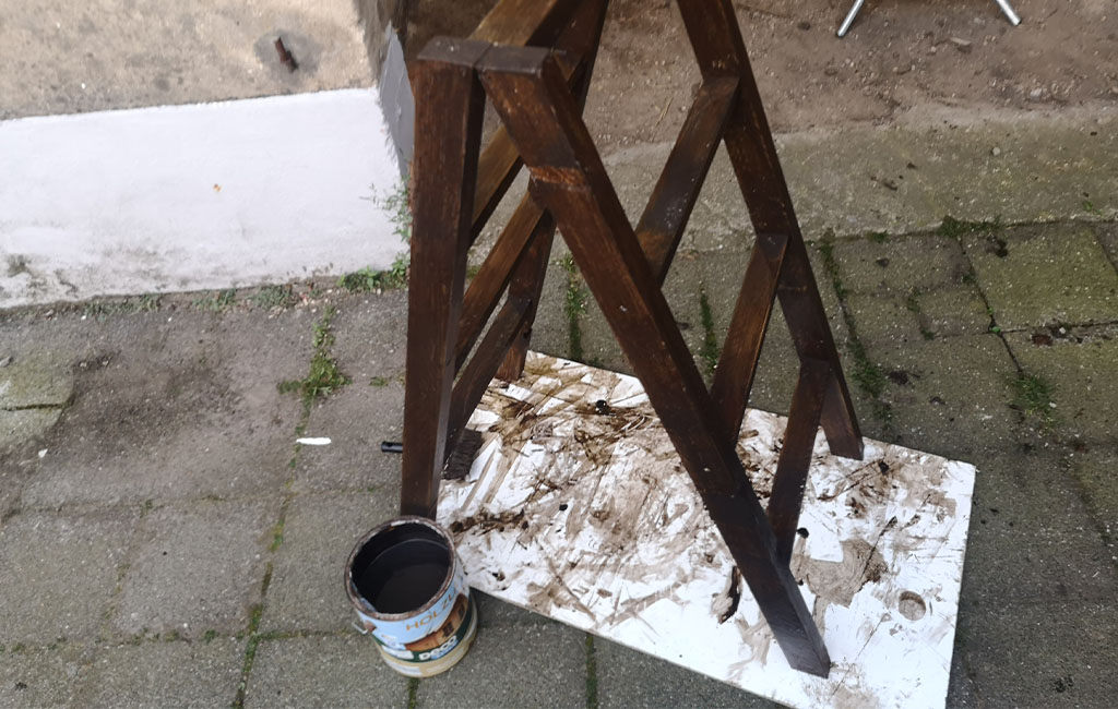 The finished painted wooden ladder stands on a white surface next to the paint can.