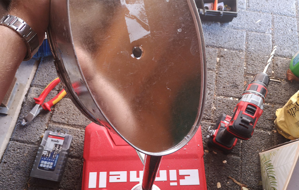 A round metal part with a large drilled hole in the center, an Einhell cordless drill lies beside it.