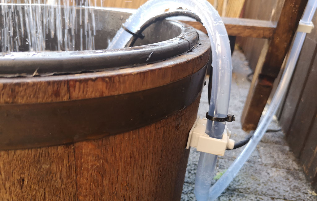 Close-up of a wooden barrel with an attached water hose and running water.