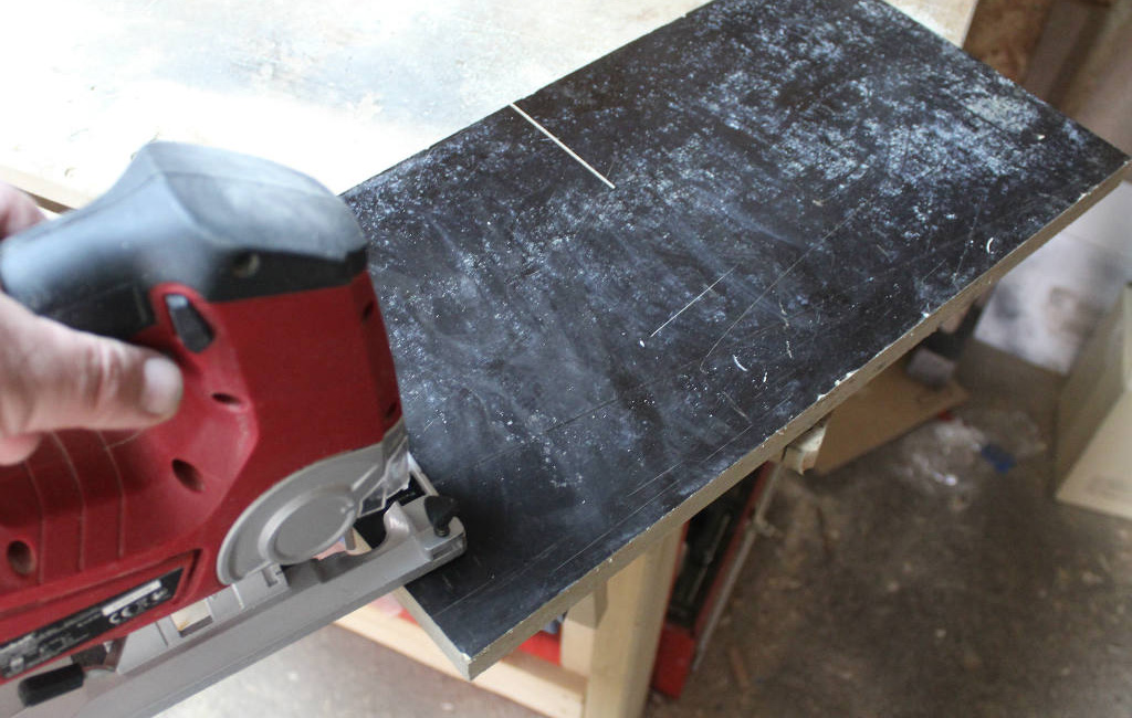 Hand guiding an Einhell jigsaw over a black board with visible cut lines.