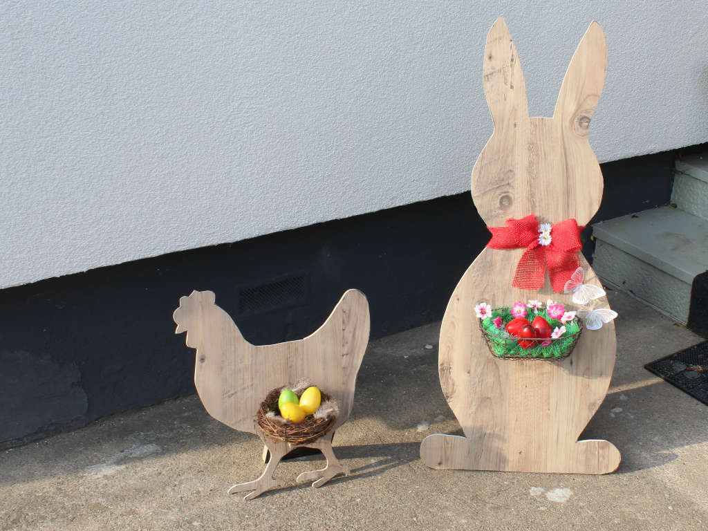 Dekorative Holzfiguren von Hahn und Hase mit Ostereiern vor einer Hauswand.