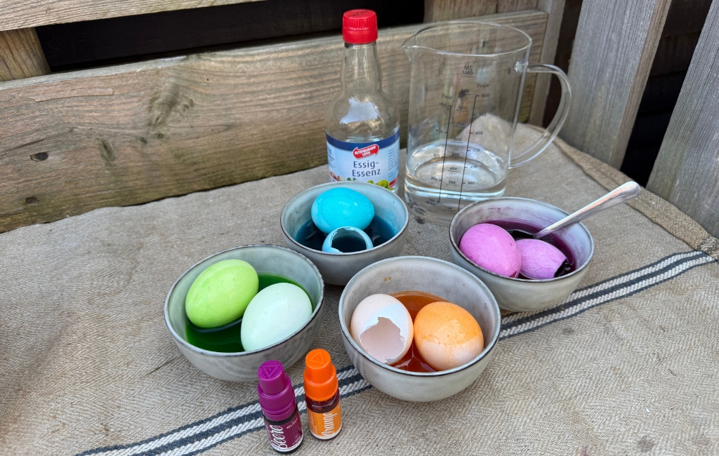 Colored eggs in bowls with dye, with small color bottles and vinegar essence next to them.