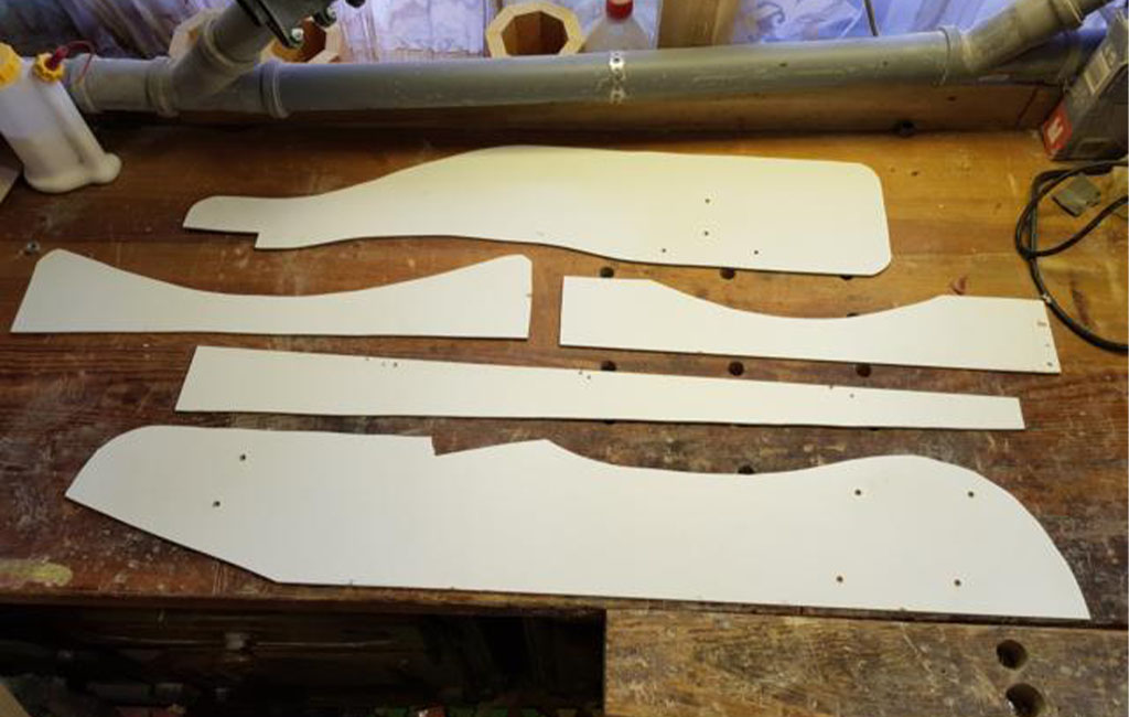 Five white wooden templates in different shapes lie next to each other on a workbench.