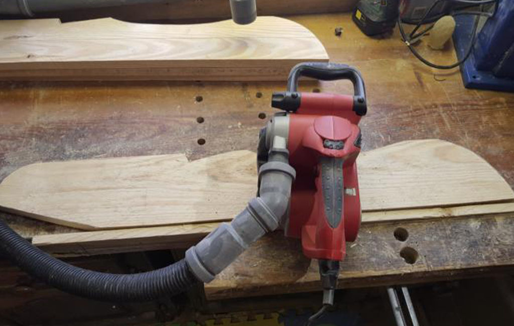An Einhell surface planer with vacuum hose lies on a cut-out wooden board.