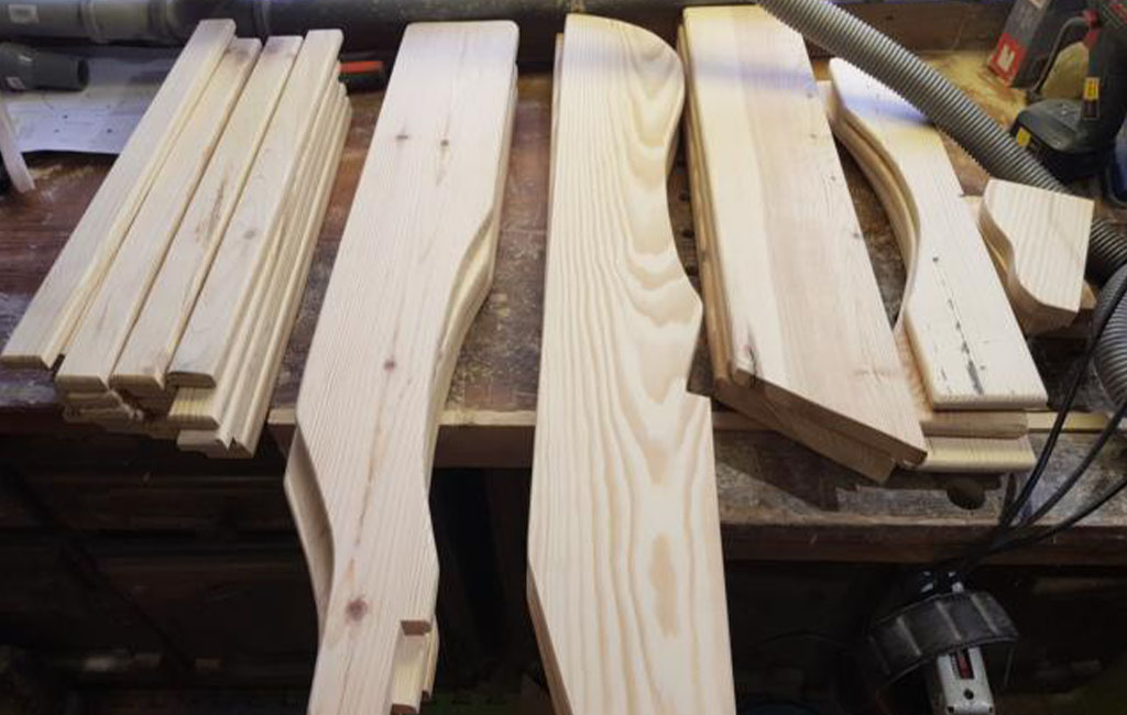 Various sawn wooden slats and curved parts lie on a workbench.