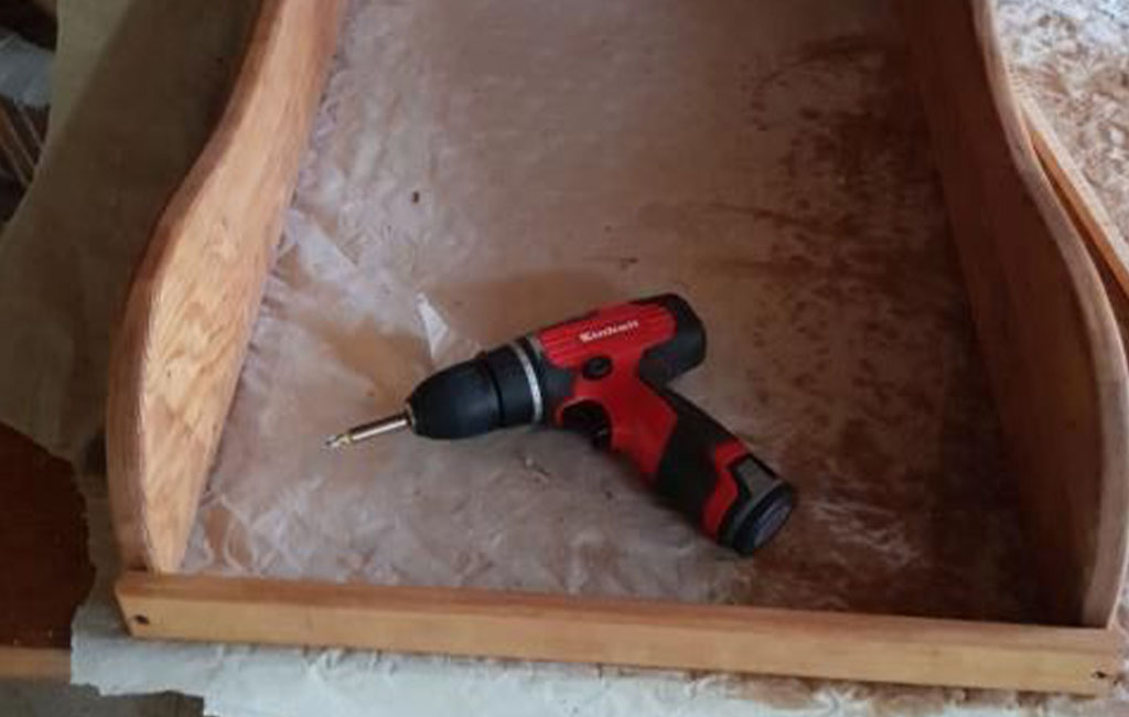 A red Einhell cordless screwdriver lies in a wooden frame on a workbench.