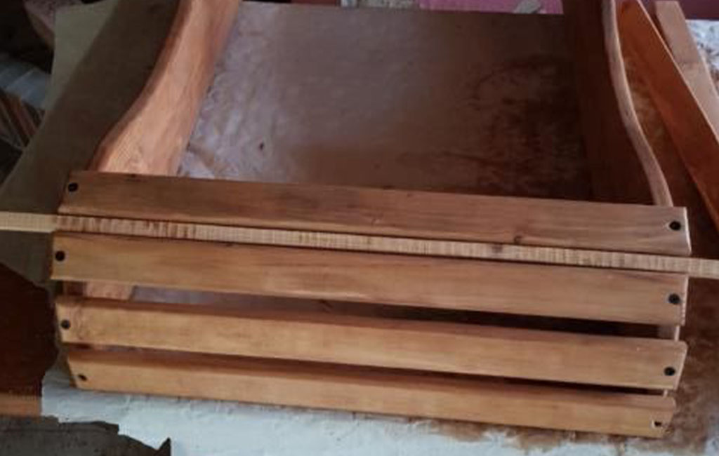 The frame of a wooden garden chair lies on a workbench, with several cross slats mounted.