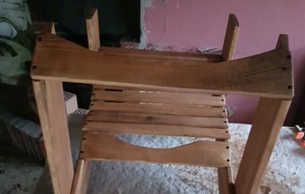 The frame of a wooden chair lies upside down, showing the slatted seat from below.
